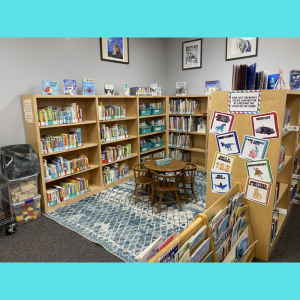 Children's reading area with bookshelves, a round table with chairs, and a patterned rug.