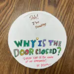 Circular sign with the phrase "WHY IS THE DOOR CLOSED?" in multicolored letters, links to more information
