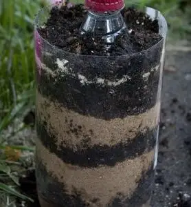 Image shows a plastic bottle layered with dirt and sand.