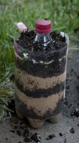 Image shows a plastic bottle layered with dirt and sand.
