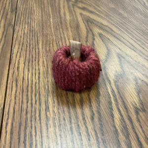 Small burgundy yarn pumpkin with a tan stem on a wood-grain table, links to more information