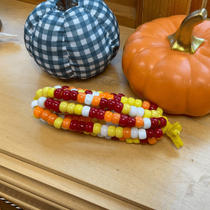 A colorful beaded corn decoration in front of two pumpkins, links to more information
