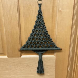 A dark green macrame pine tree hanging on a wooden door, links to more information